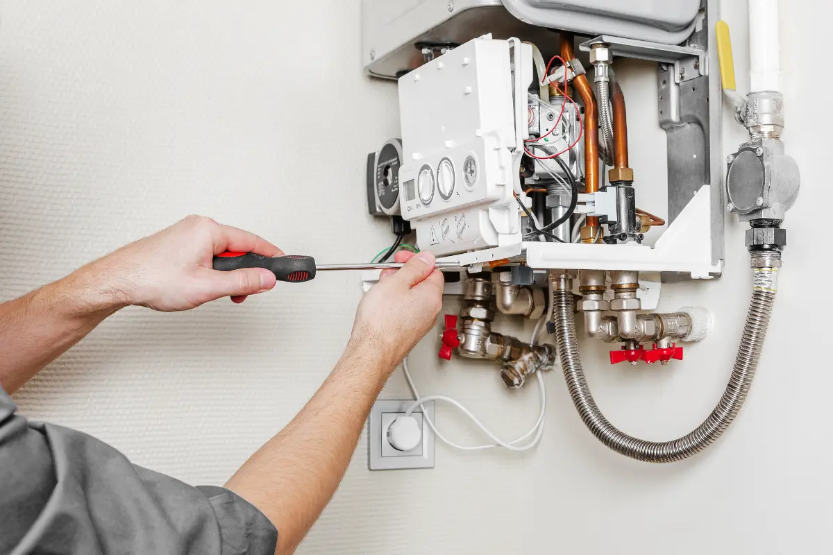 Instalator podłącza i reguluje kocioł gazowy. Po prawej stronie kotła widoczne jest podłączenie do gazu (zawór z żółtą rączką)